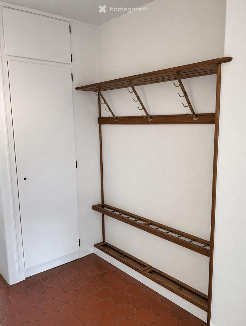Empty hallway with white walls, red hexagonal tiles, and a wooden coat rack with hooks and shelves.