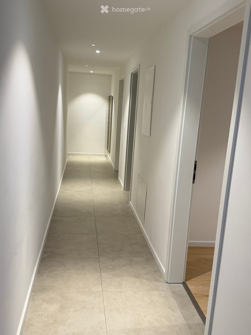 Clean, modern hallway with white walls, tiled floor, and several doors leading to rooms.