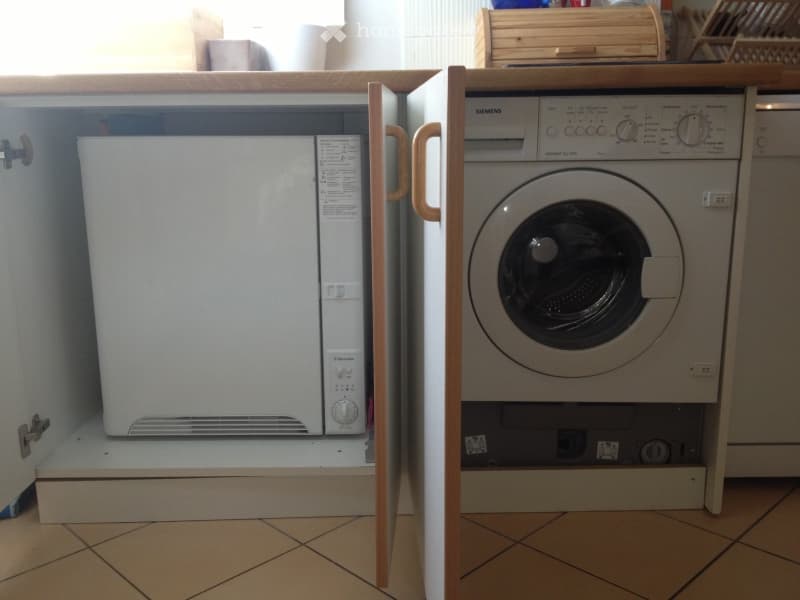 A small bathroom with a washing machine and microwave, both integrated into wooden cabinetry.