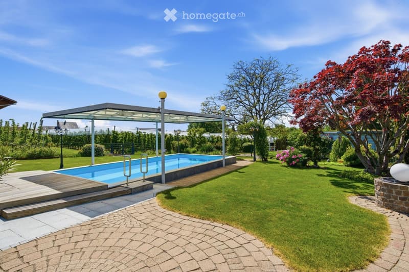 Well-maintained garden with a swimming pool, covered patio, lush greenery, and a stone pathway.