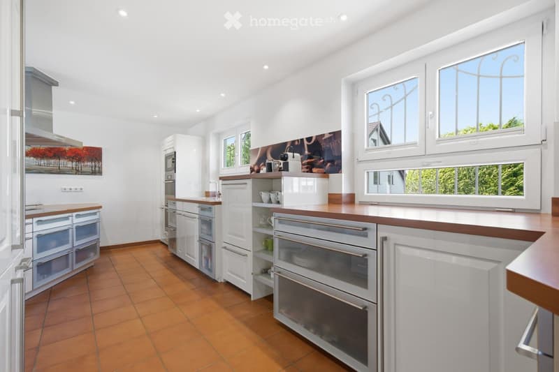 Modern kitchen with white cabinets, wooden countertops, and stainless steel appliances. Features include a microwave, oven, refrigerator, and a coffee maker on the counter.
