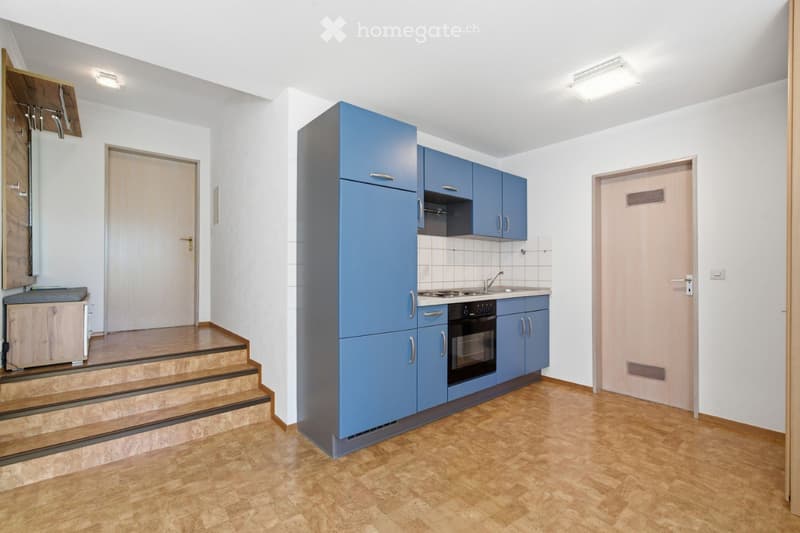 Modern kitchen with blue cabinets, a refrigerator, oven, and sink. Wooden flooring and white walls.