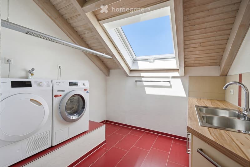 Modern bathroom with red tiled floor, white walls, skylight window, washing machine, dishwasher, and stainless steel sink.