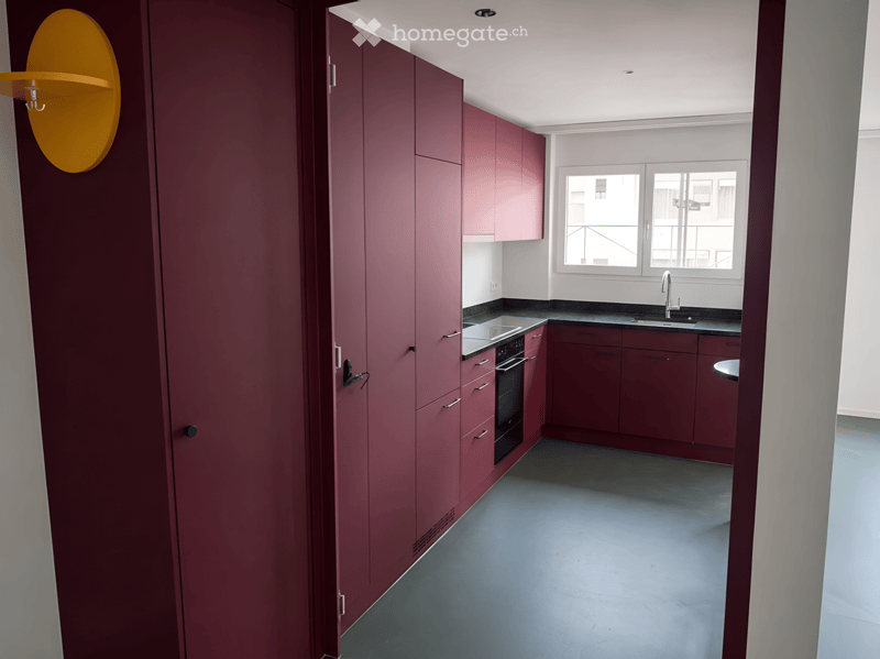 Modern kitchen with dark red cabinets, stainless steel sink, and oven. The space features a sleek design with a large window providing natural light.