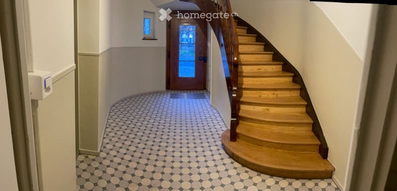 Hallway with a wooden staircase, hexagonal tile floor, and a door with a glass panel at the end.