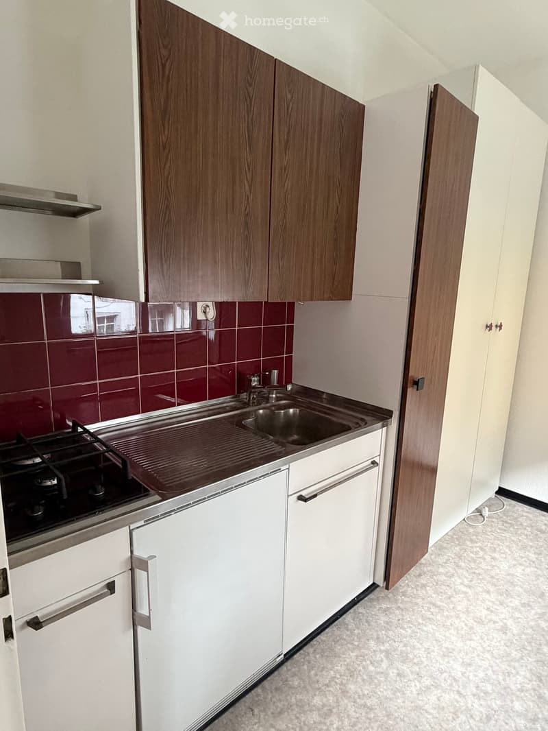 Modern kitchen with white and wood cabinets, a gas stove, a sink, and red tiled backsplash.