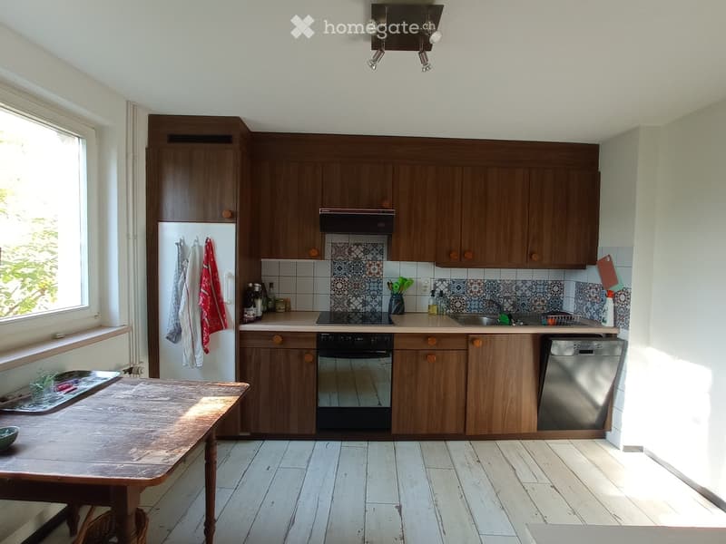 Wooden cabinets, white floor, stainless steel oven and dishwasher, sink, window with view outside, ceiling lamps