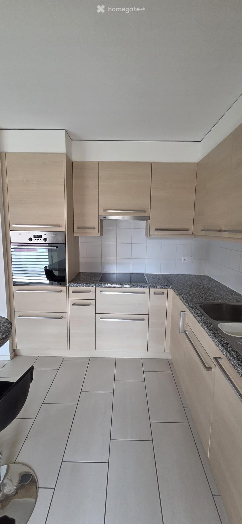 Modern kitchen with light wood cabinets, stainless steel appliances, granite countertops, and tiled flooring.
