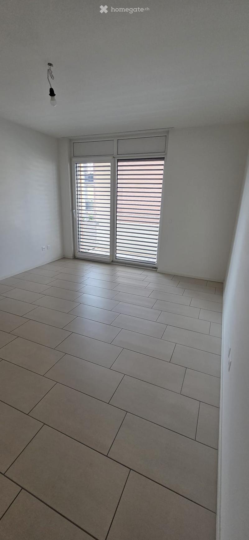 Empty room with tiled floor, white walls, and a large window with blinds. No furniture or equipment is present.