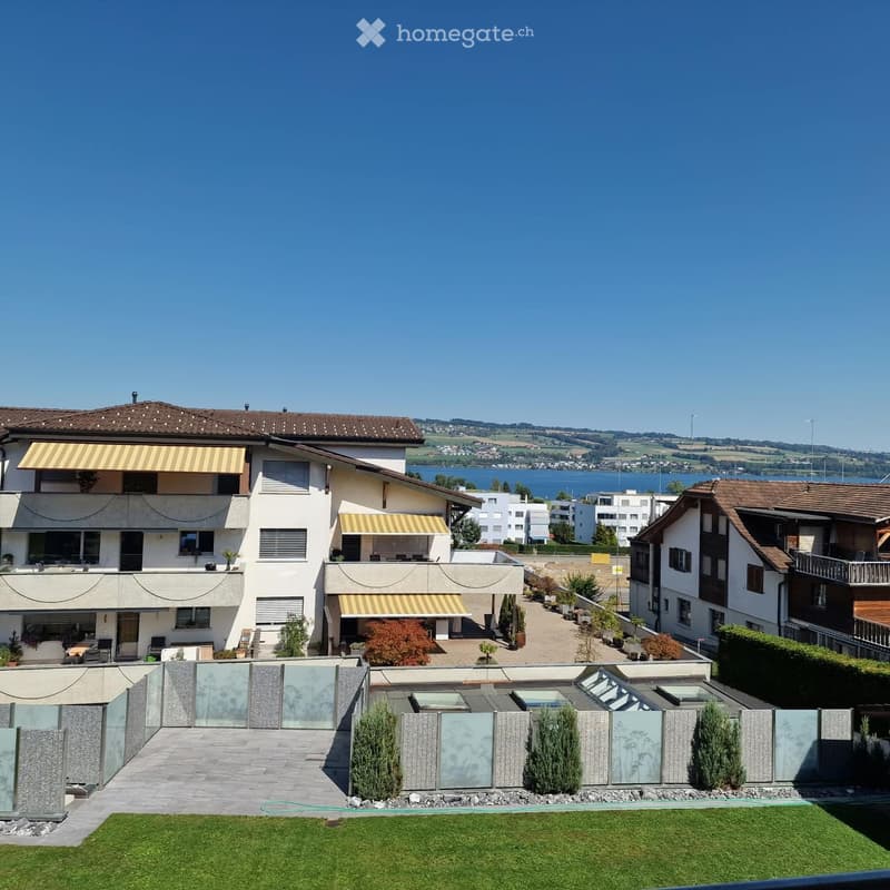 Two-story house with balconies, awnings, and a view of a lake in the background. The house features a modern design with large windows and a well-maintained garden area.