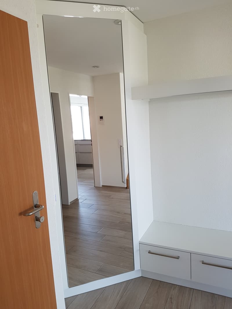 Empty hallway with wooden flooring, white walls, and a small white cabinet with drawers on the right side.