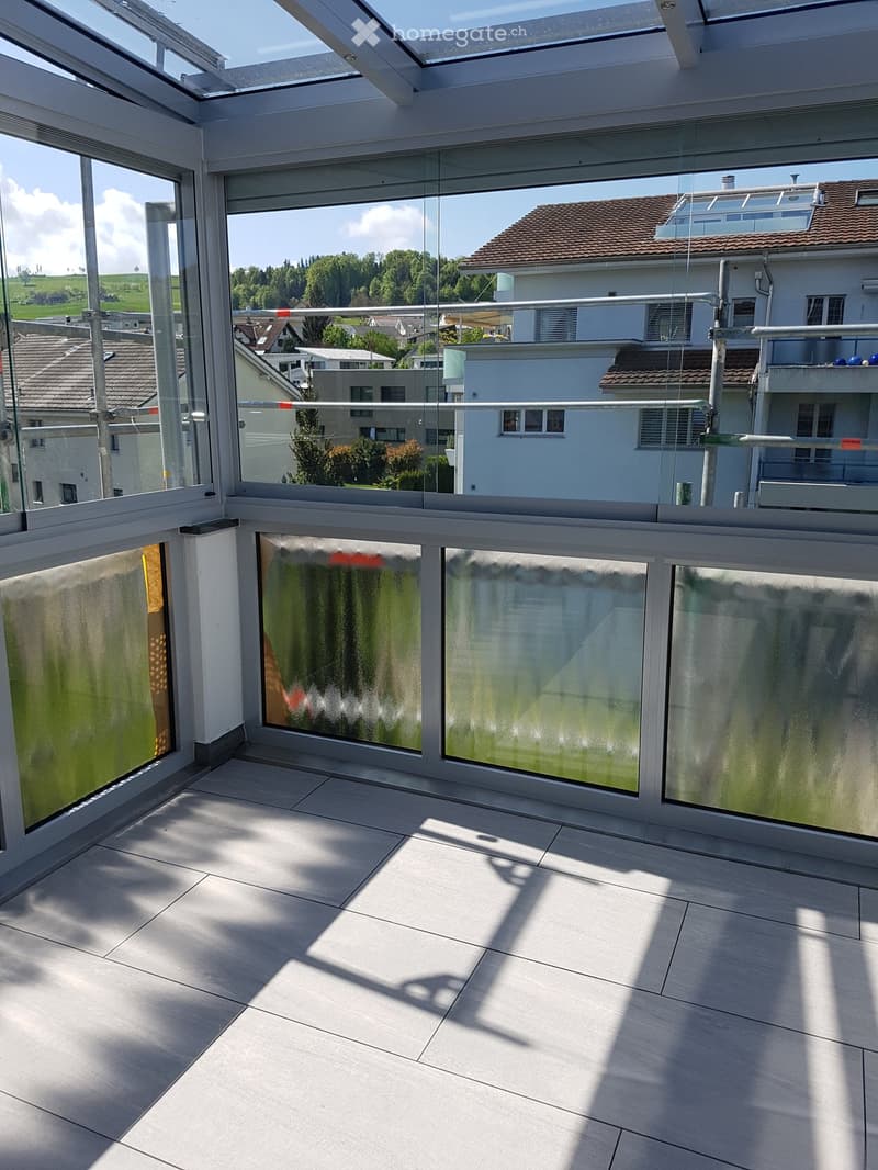 Spacious balcony with large glass panels, modern railing, and a view of the surrounding neighborhood and countryside.