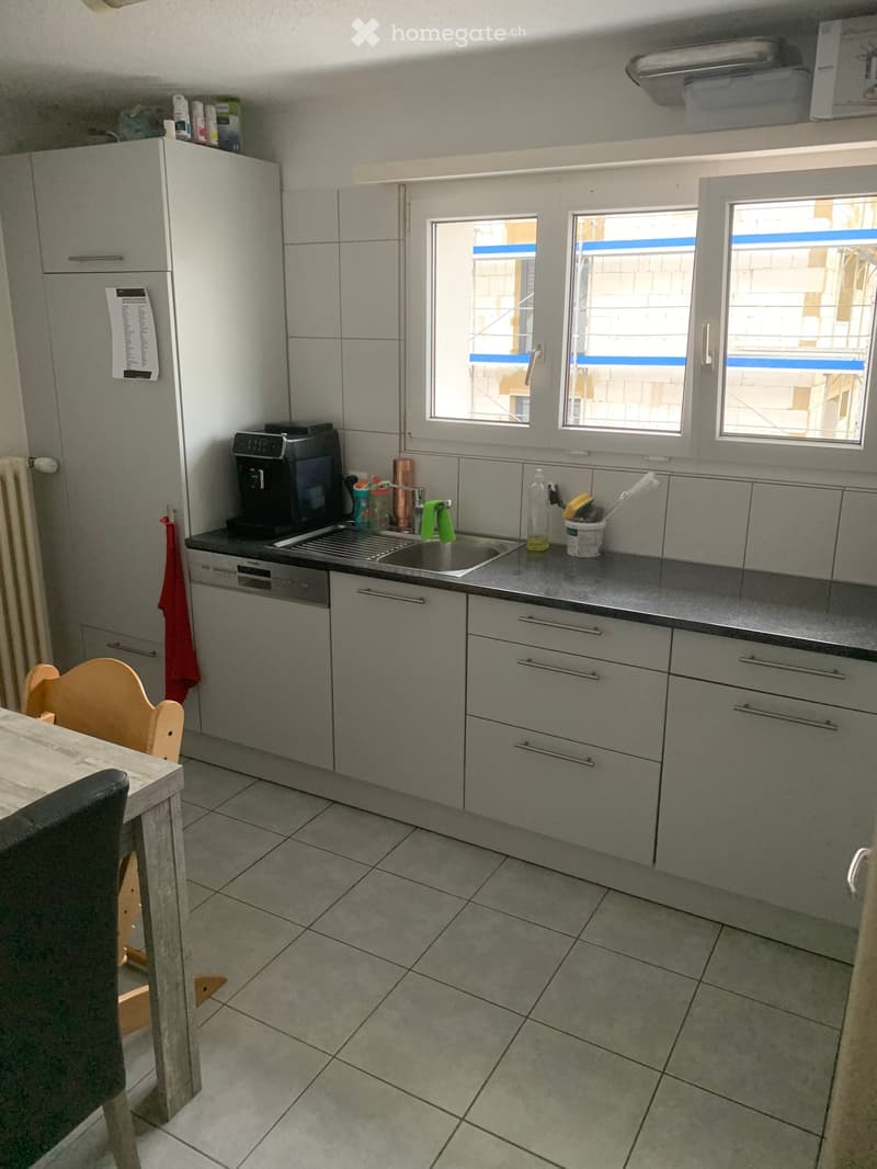 Modern kitchen with grey cabinets, stainless steel appliances, tiled floor, and a small dining area with a wooden table and chairs.