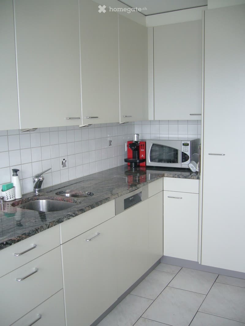 Modern kitchen with white cabinets, granite countertop, stainless steel sink, microwave, and coffee maker.