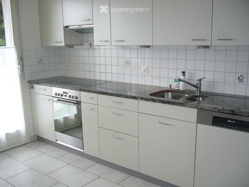 Modern kitchen with white cabinets, granite countertop, stainless steel sink, oven, and dishwasher.