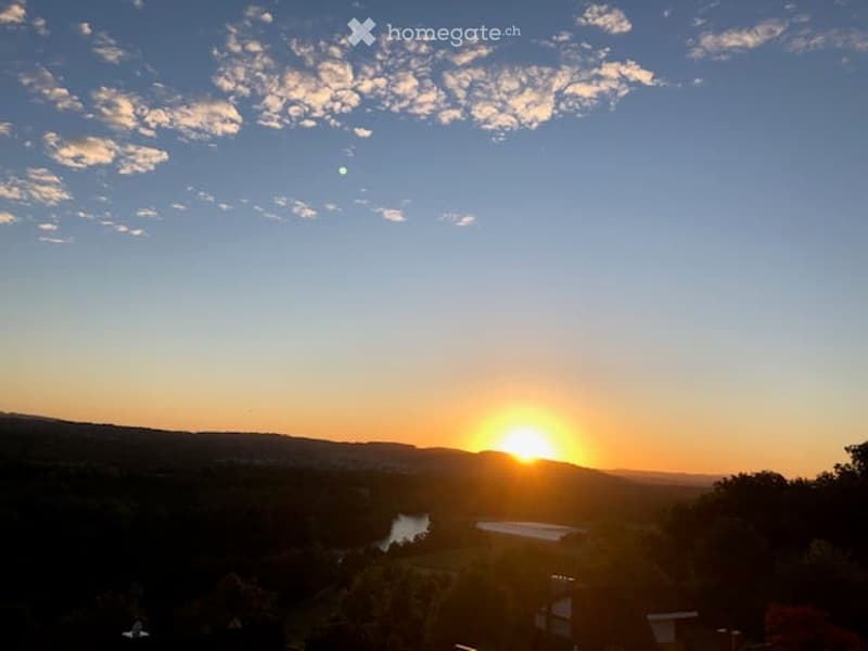 Scenic view of a sunset over a valley with a river and distant hills, with a small structure visible in the foreground.