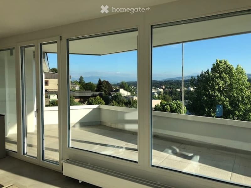 Bright, modern balcony with large glass doors, tiled floor, and scenic view of the city and mountains.