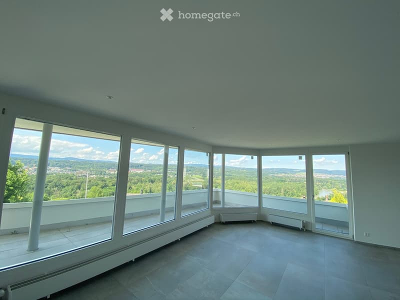 Bright, empty room with large windows offering a scenic view of a green landscape and distant cityscape. The room features a tiled floor and white walls.
