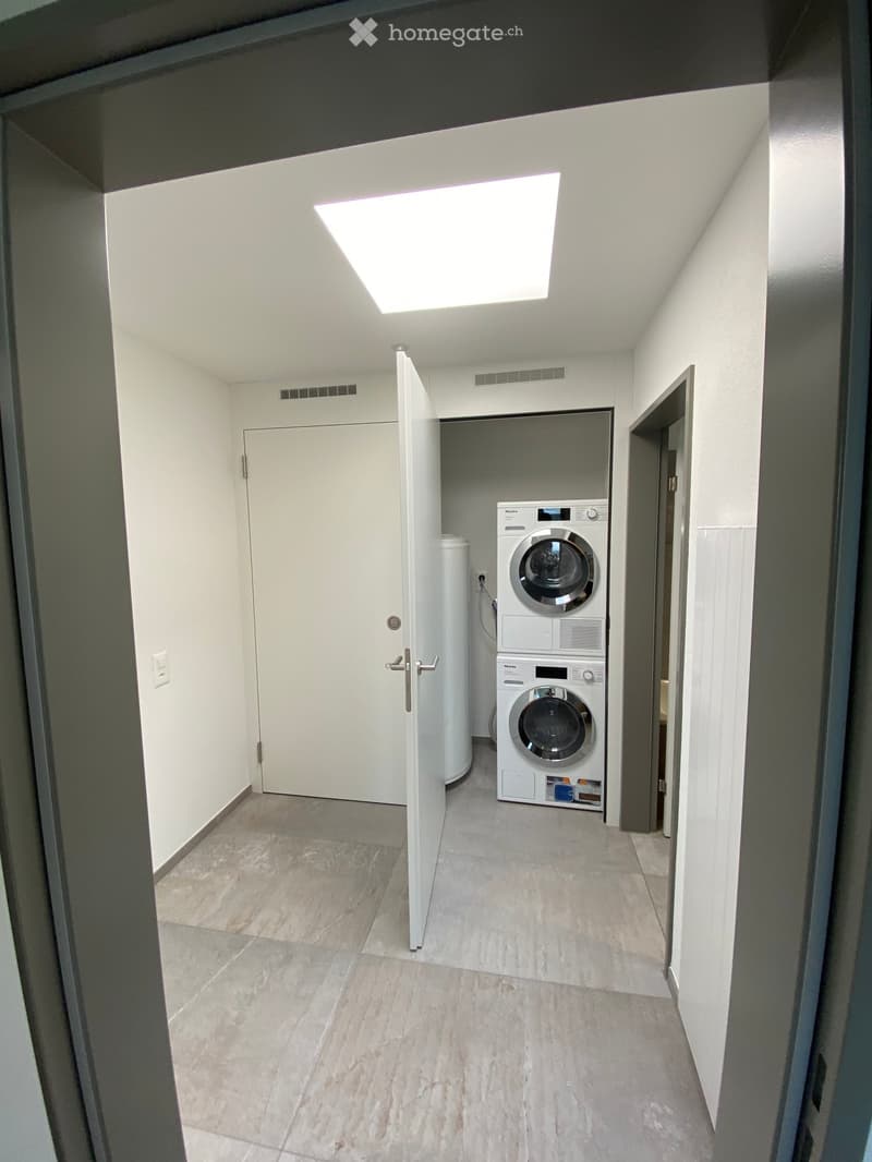 Clean, modern hallway with tiled floor, white walls, and a private washing machine in an adjacent room.