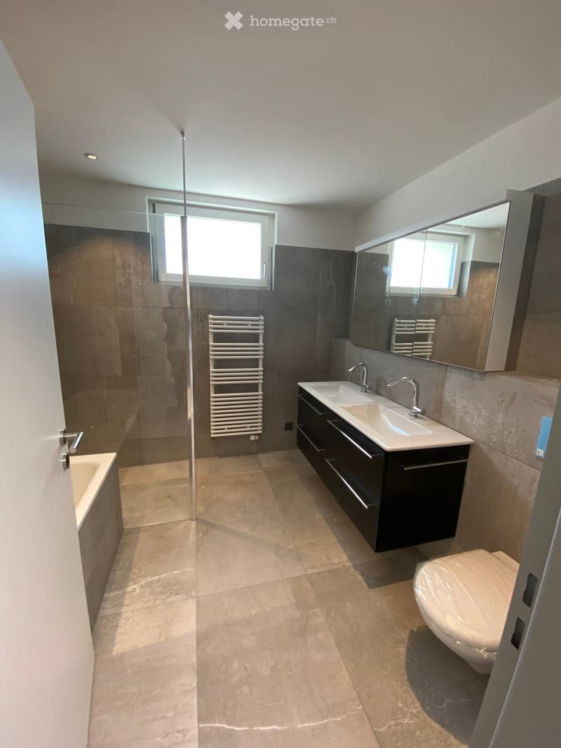 Modern bathroom with beige tiles, double sink, large mirror, toilet, bathtub, and a radiator near the shower area.