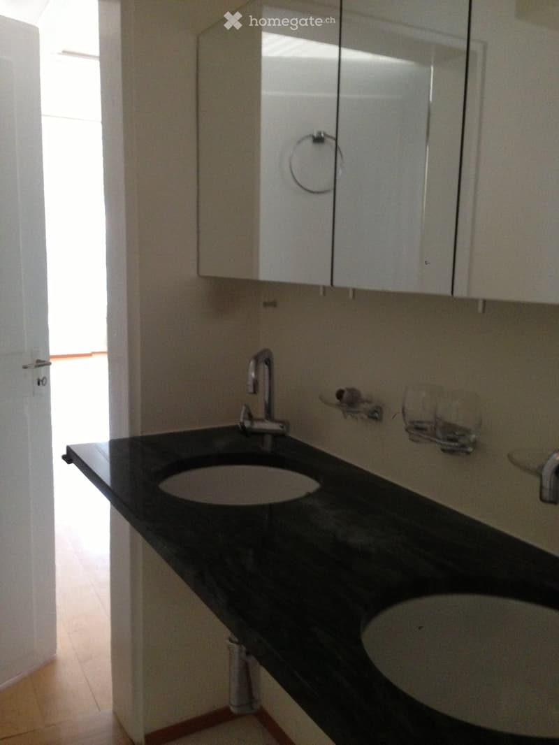Modern bathroom with a black countertop, two sinks, a mirror, and white cabinets.