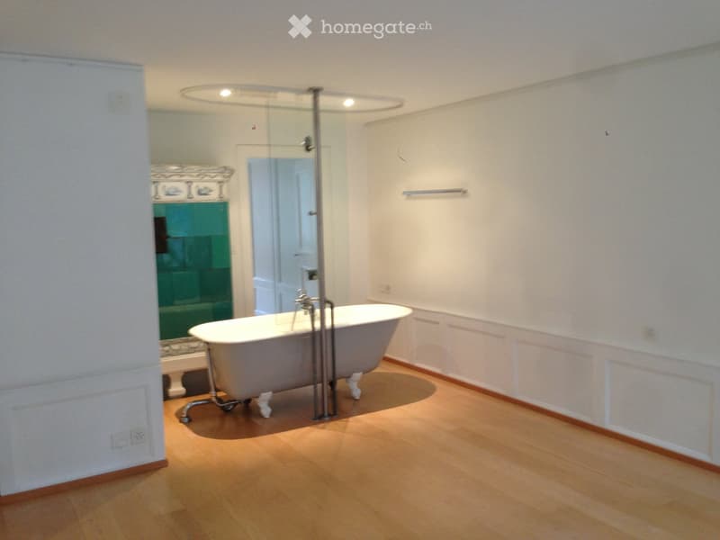 Bathroom with a freestanding bathtub, glass shower enclosure, and a decorative mirror. Light wooden flooring and white walls.