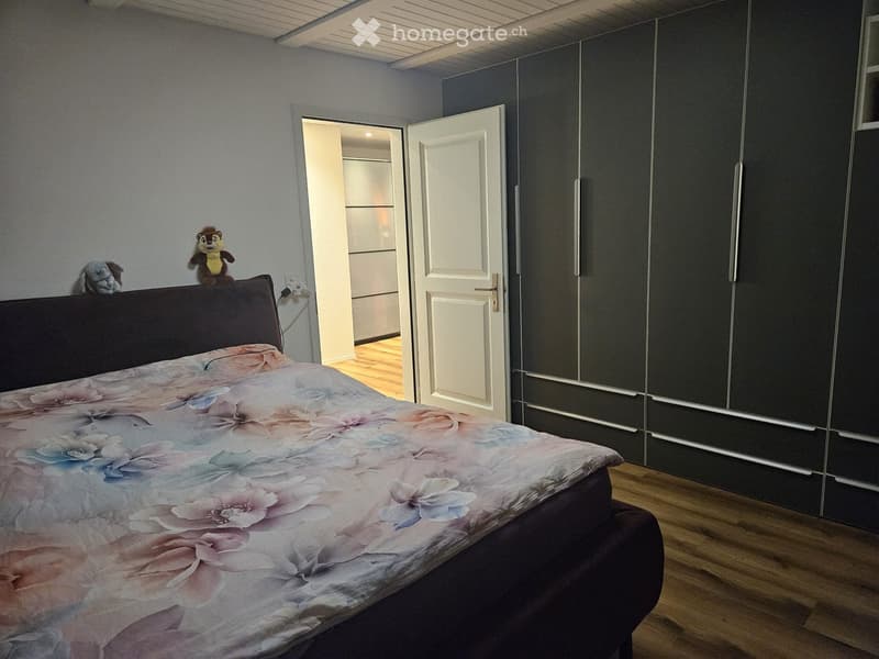 Bedroom with a large bed, floral duvet, dark wooden wardrobe, and two stuffed toys on the headboard.