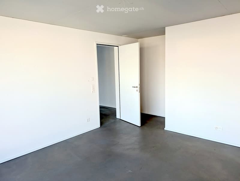 Empty room with white walls, concrete floor, and a single open door leading to another space.