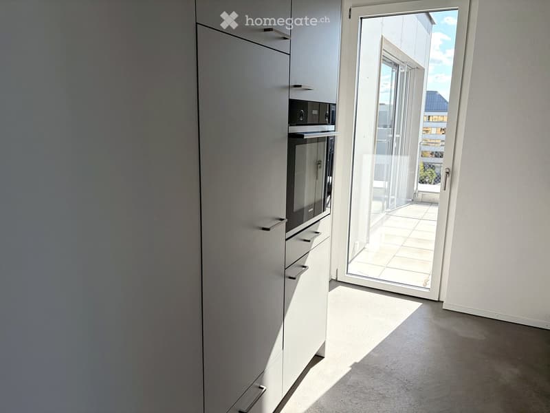 Modern kitchen with white cabinets, built-in oven, and a sliding glass door leading to a balcony.