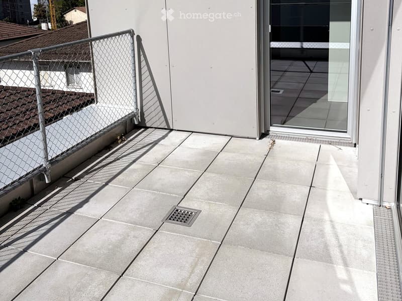 Modern balcony with concrete tiles, metal railing, and a sliding glass door leading inside.