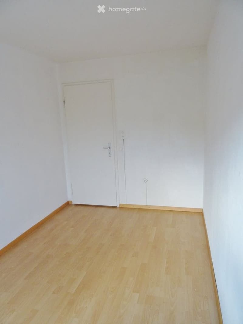 Empty room with light wooden flooring and white walls, featuring a single white door.