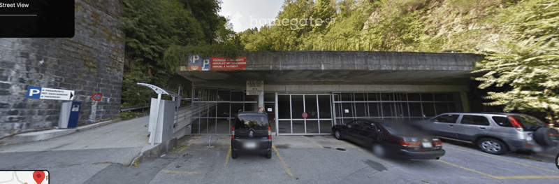 Parking area with several cars, entrance gate, and signage indicating parking availability.