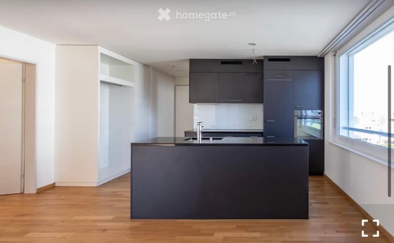 Modern kitchen with dark cabinets, a central island, and a sink, featuring large windows and wooden flooring.