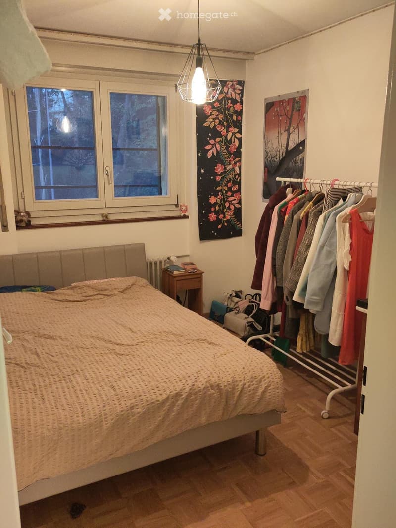 Bedroom with a bed, nightstand, radiator, clothing rack, and artwork on the walls.