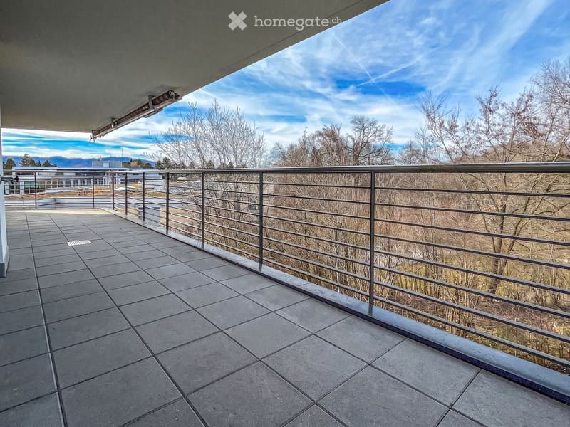 Balcony with tiled floor, metal railing, and scenic view of trees and mountains under a partly cloudy sky.