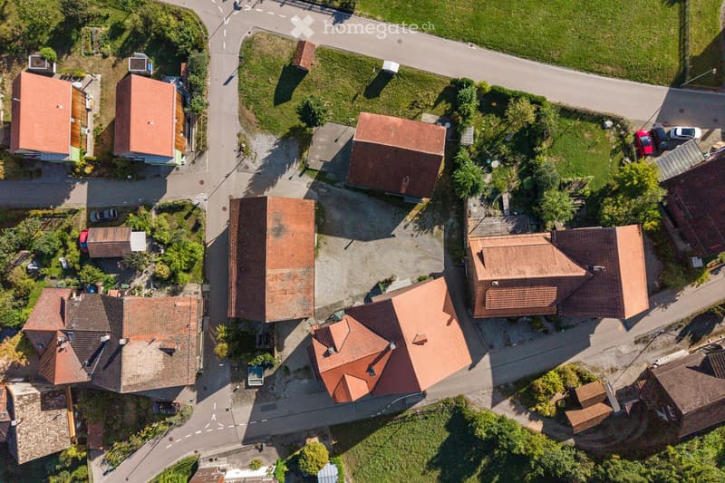 Aerial view of a residential neighborhood with multiple houses featuring red-tiled roofs, surrounded by greenery and roads.