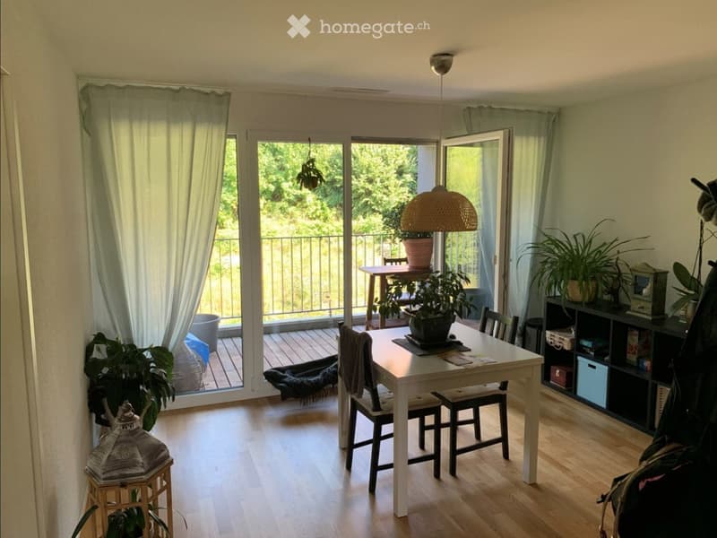 Bright dining area with a white table, four chairs, and potted plants. Large sliding glass doors open to a balcony with outdoor furniture and greenery.
