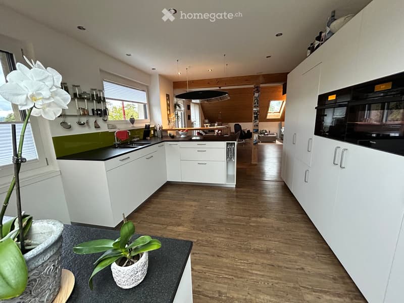 Modern kitchen with white cabinets, black countertops, and wooden flooring. Features a sink, faucet, oven, and potted plants on the counter.