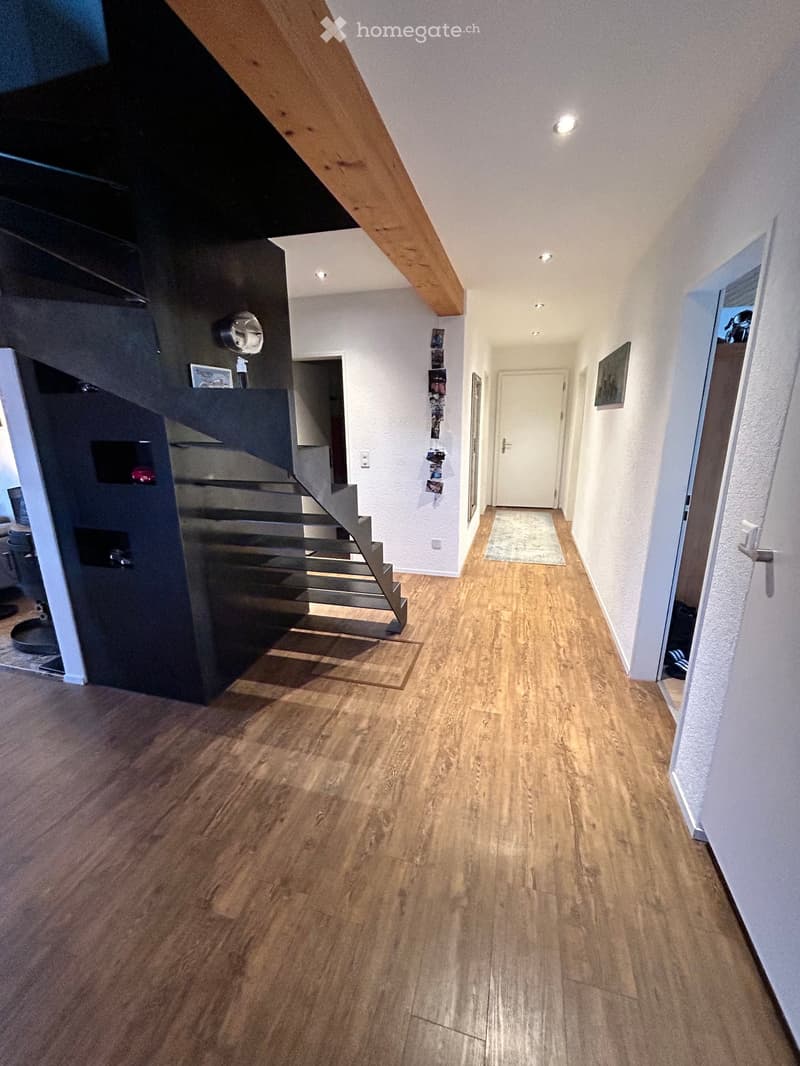 Modern hallway with wooden flooring, white walls, recessed lighting, and a staircase leading upwards.