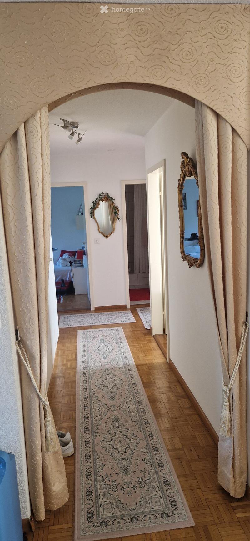 Elegant hallway with wooden flooring, ornate curtains, and decorative mirrors. Features a long runner rug and several smaller rugs leading to adjacent rooms.