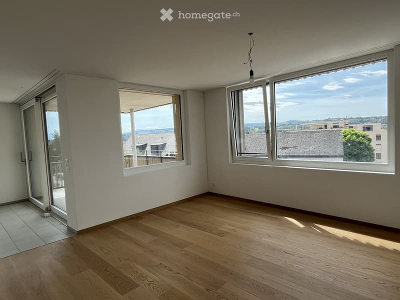 Empty room with wooden flooring, large windows, and a sliding glass door leading to a balcony.