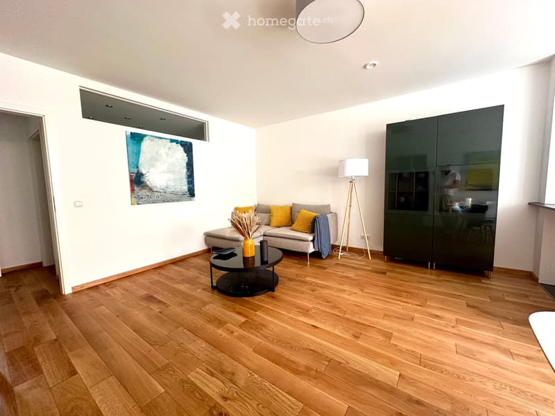 Modern living room with light wooden flooring, a grey sofa with yellow cushions, a black coffee table with a vase, a floor lamp, and a dark green cabinet.