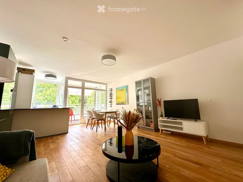 Modern living room with wooden flooring, large windows, a sofa, coffee table, TV, dining area, and decorative vases.