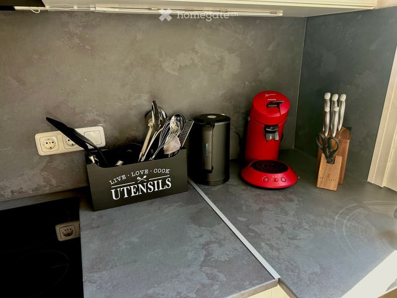 Modern kitchen with grey concrete countertops, stainless steel appliances, and organized storage for utensils and kitchen tools.