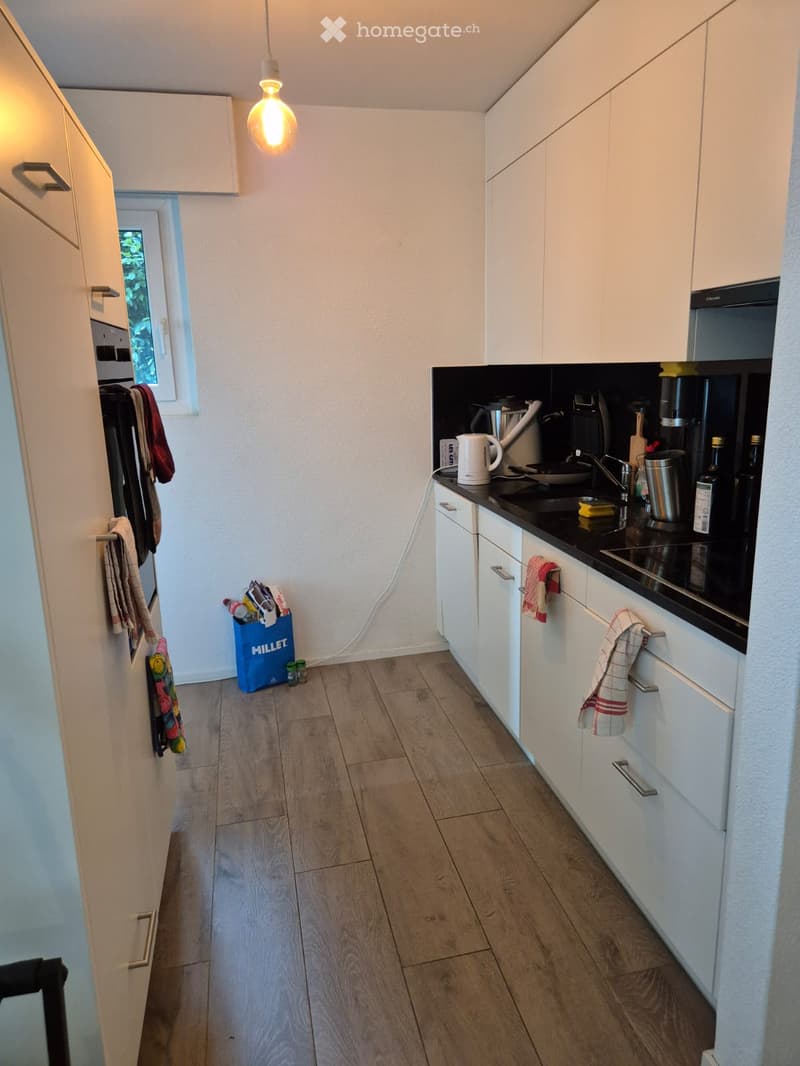 Modern kitchen with white cabinets, black countertop, wooden floor, and various appliances including a coffee maker, sink, and oven.