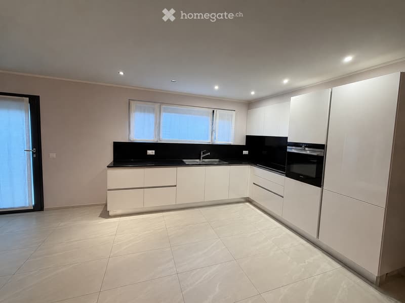 Modern kitchen with white cabinets, black countertops, and a built-in oven. Features a large window and recessed lighting.