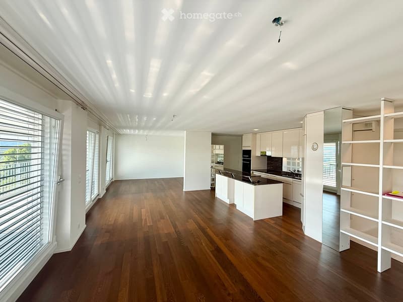 Bright, open-plan living and dining area with hardwood flooring, large windows with blinds, and a modern kitchen with white cabinets and a central island.