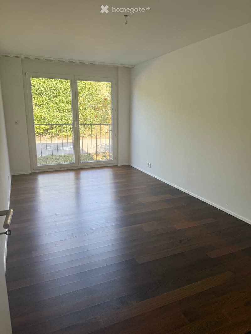 Empty room with wooden flooring, white walls, and large sliding glass doors leading to a balcony.