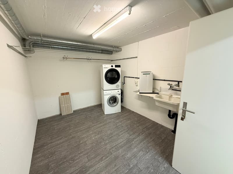 A small utility room with a washing machine, dishwasher, and sink, featuring white walls and a wooden floor.