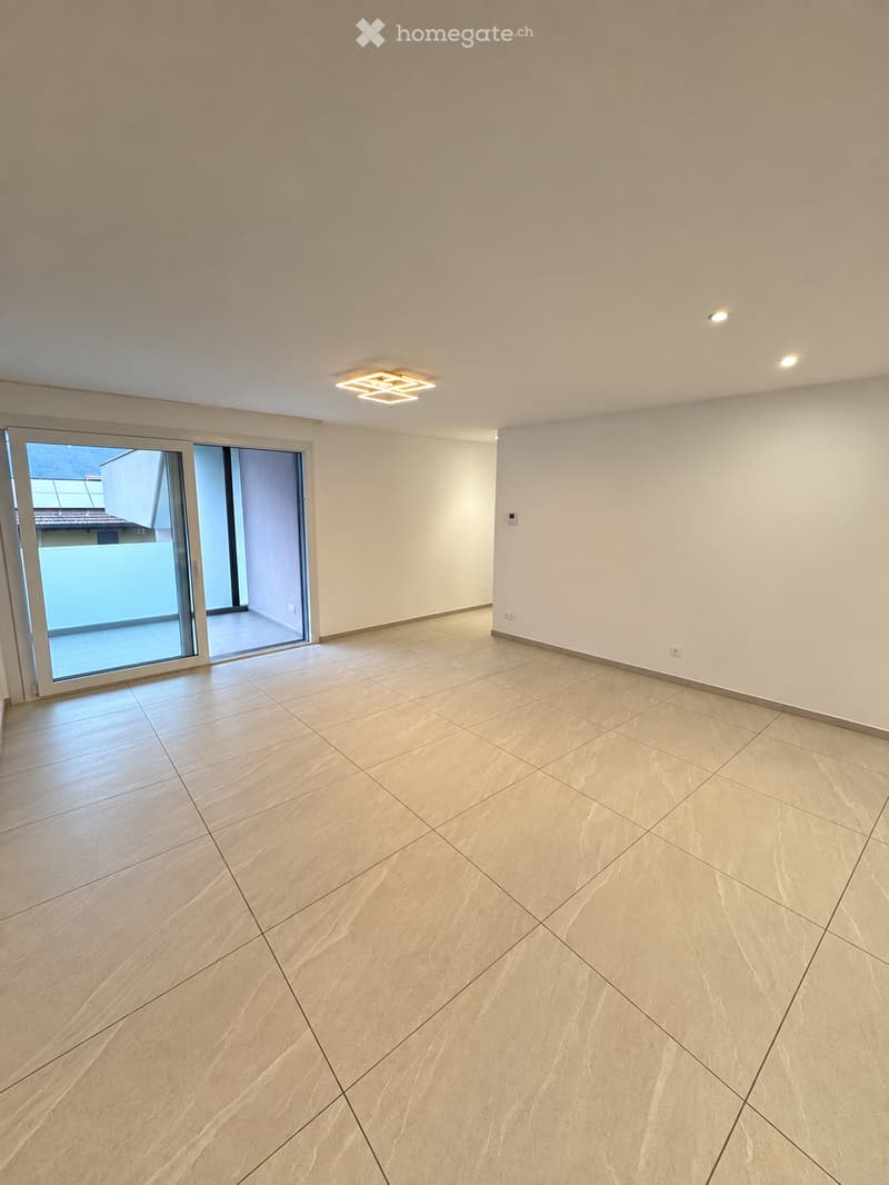 Empty room with light-colored tiled flooring, white walls, and a large sliding glass door leading to a balcony or outdoor area.